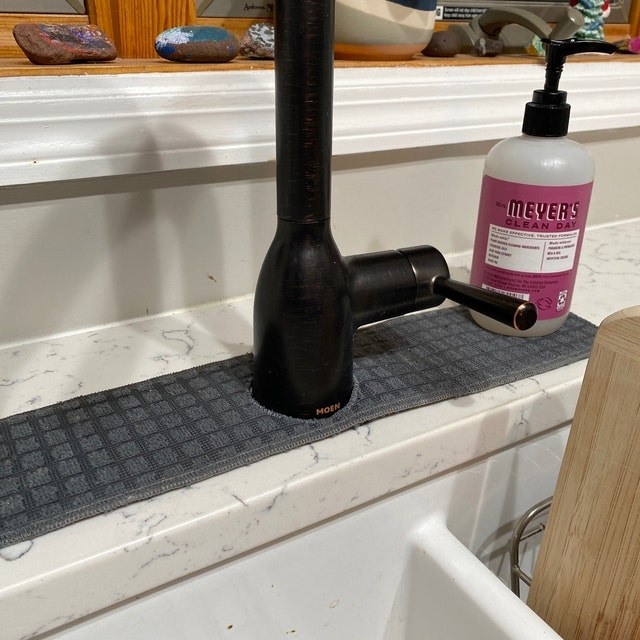 reviewer&#x27;s photo of the faucet splash catcher in gray around a faucet