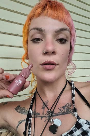 a reviewer wearing a light pink shade and holding the bottle