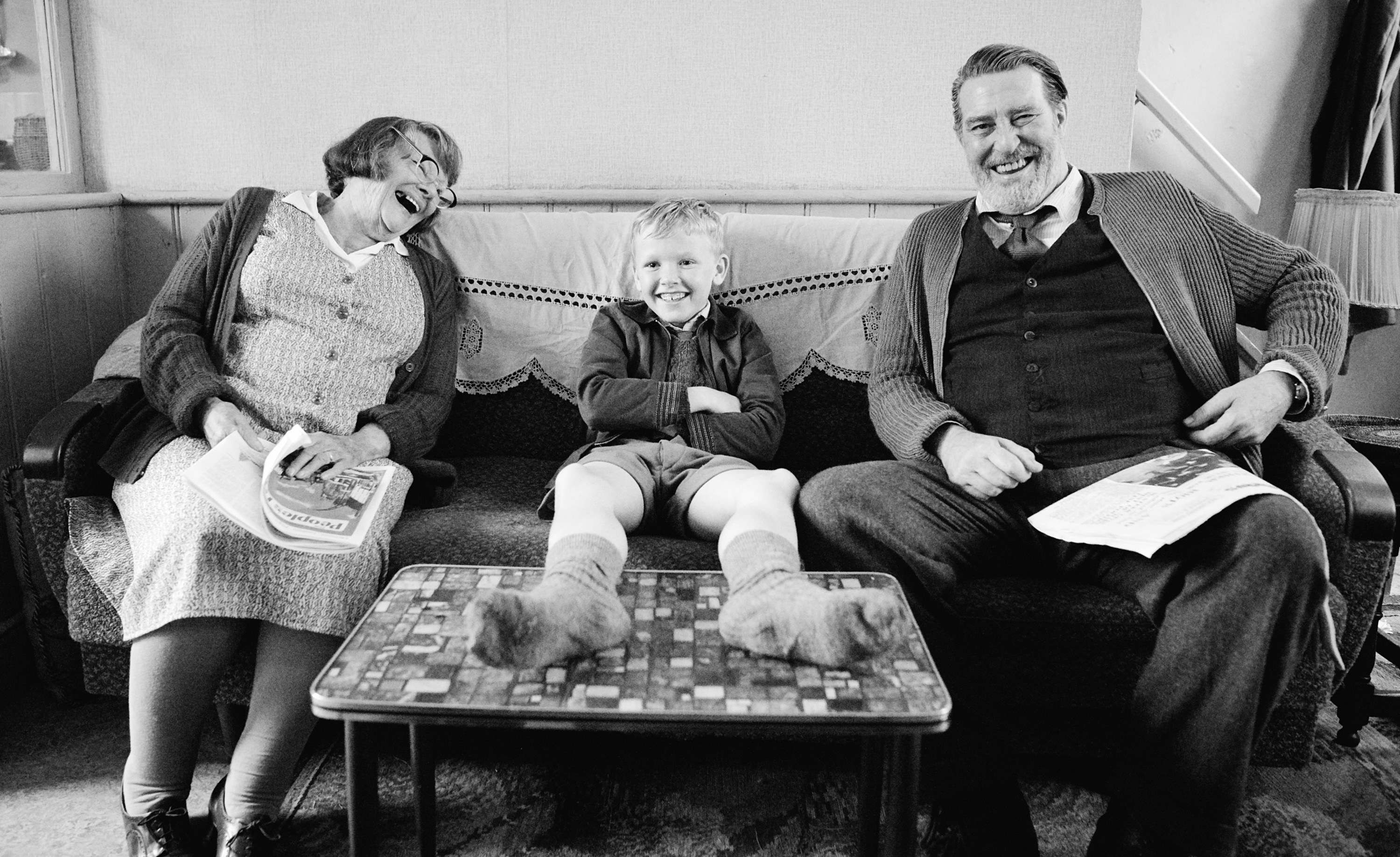 Judi Dench, Jude Hill, and Ciaran Hinds laugh together on a couch