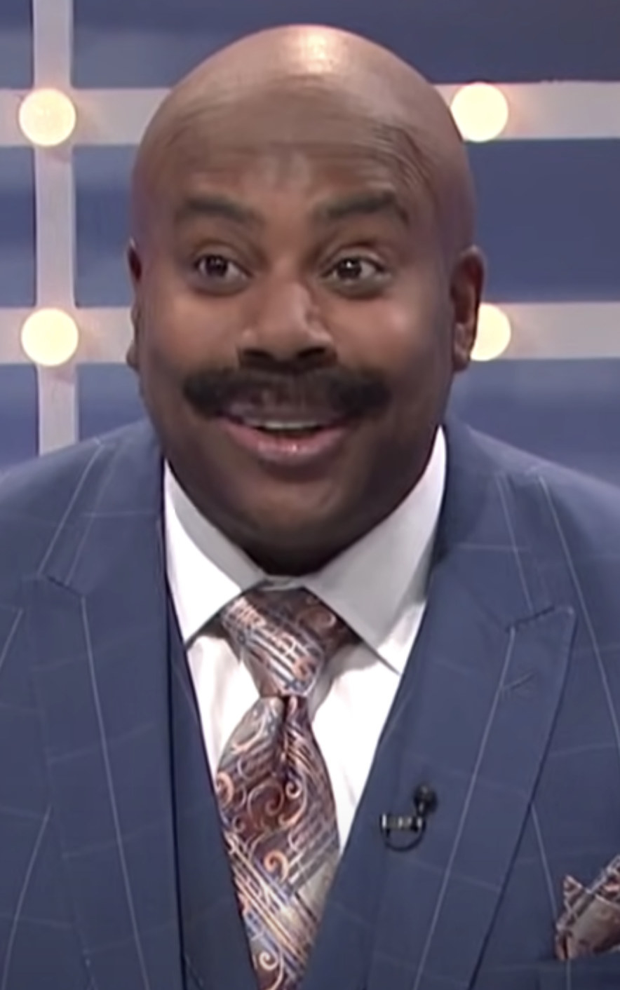 Thompson wearing a bald cap, mustache, and suit like Steve Harvey