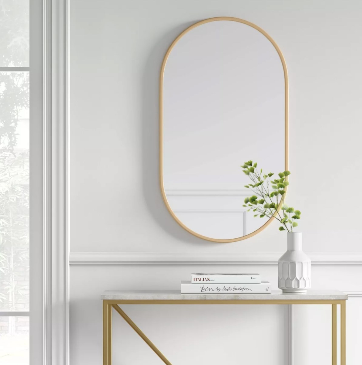 The brass oval mirror is hung in a bright white room