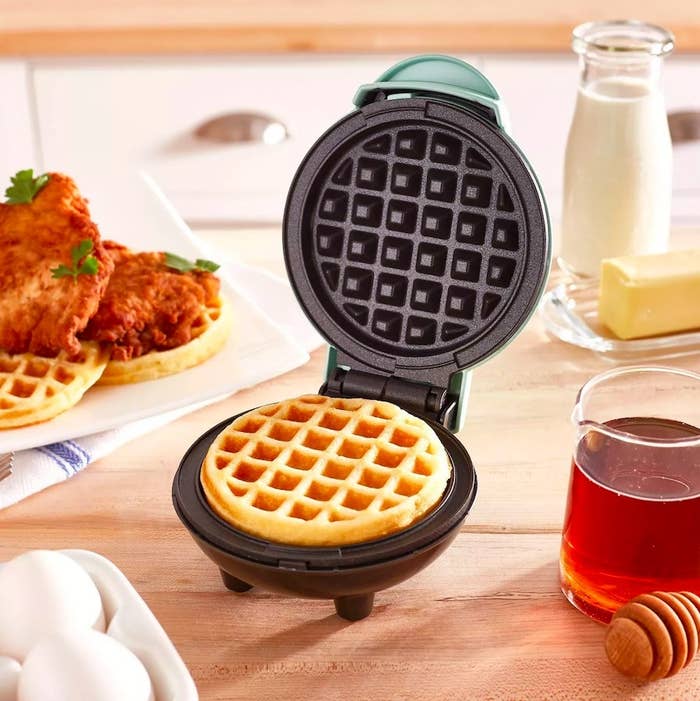 Waffle maker next to plate of chicken and waffles and various ingredients
