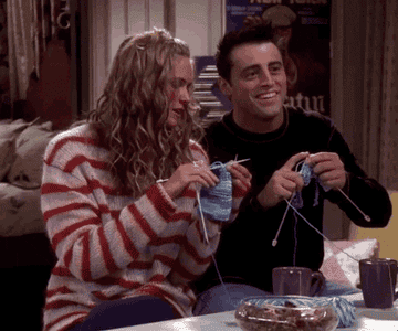 Joey and his girlfriend in &quot;Friends&quot; knitting together, smiling. They are sat at the kitchen counter and Joey is wearing a black jumper and jeans while his girlfriend is wearing a stripy red jumper and jeans.