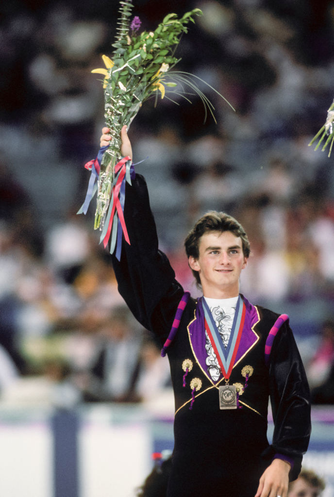 Todd is holding up flowers in 1990 with his medal around his neck