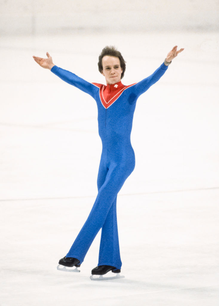 Scott is in a skin-tight skating costume as he raises his arms and acknowledges the crowd