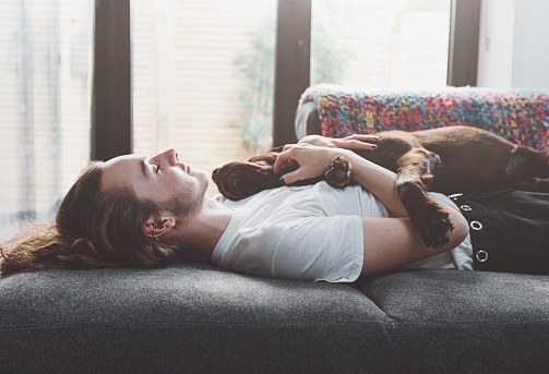Young man lies on couch with dog