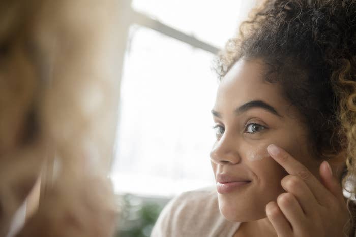 A person putting face cream on in a mirror.