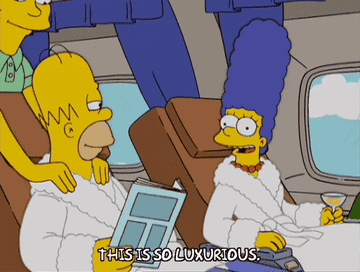 a gif of Marge in &quot;The Simpsons&quot; sitting on an airplane, raising a champagne glass and saying &quot;this is so luxurious&quot;