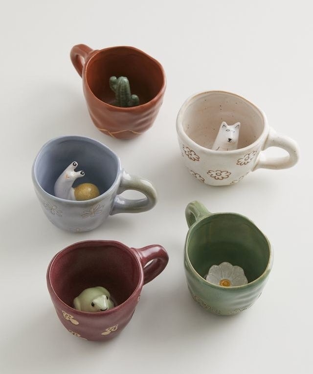 Five ceramic mugs with hidden critters and plants inside