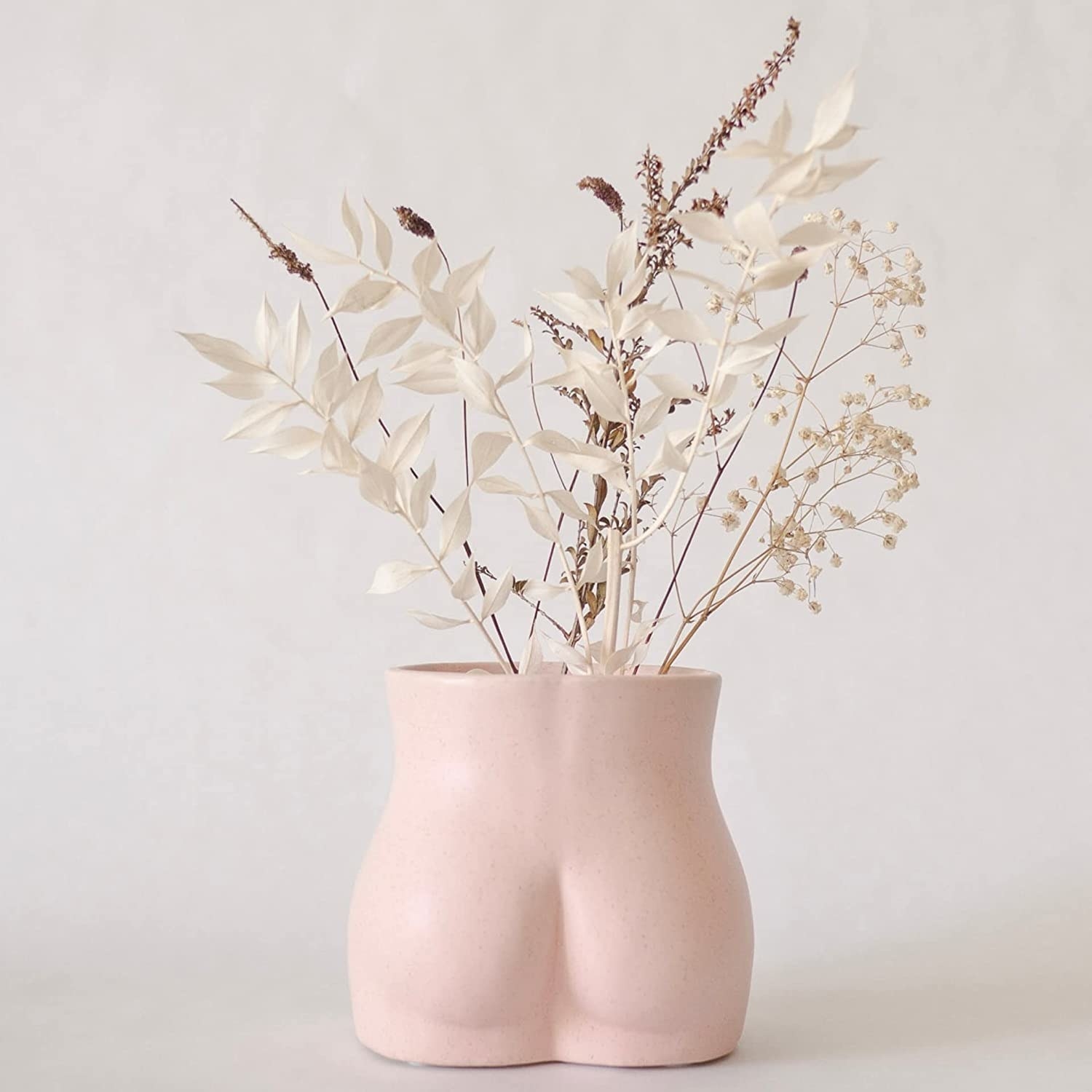 The butt-shaped vase holding some dried flowers in front of a plain background