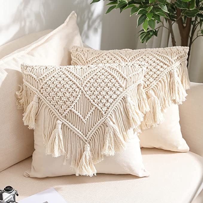 A set of two pillows on a couch that both have the macrame cases on them