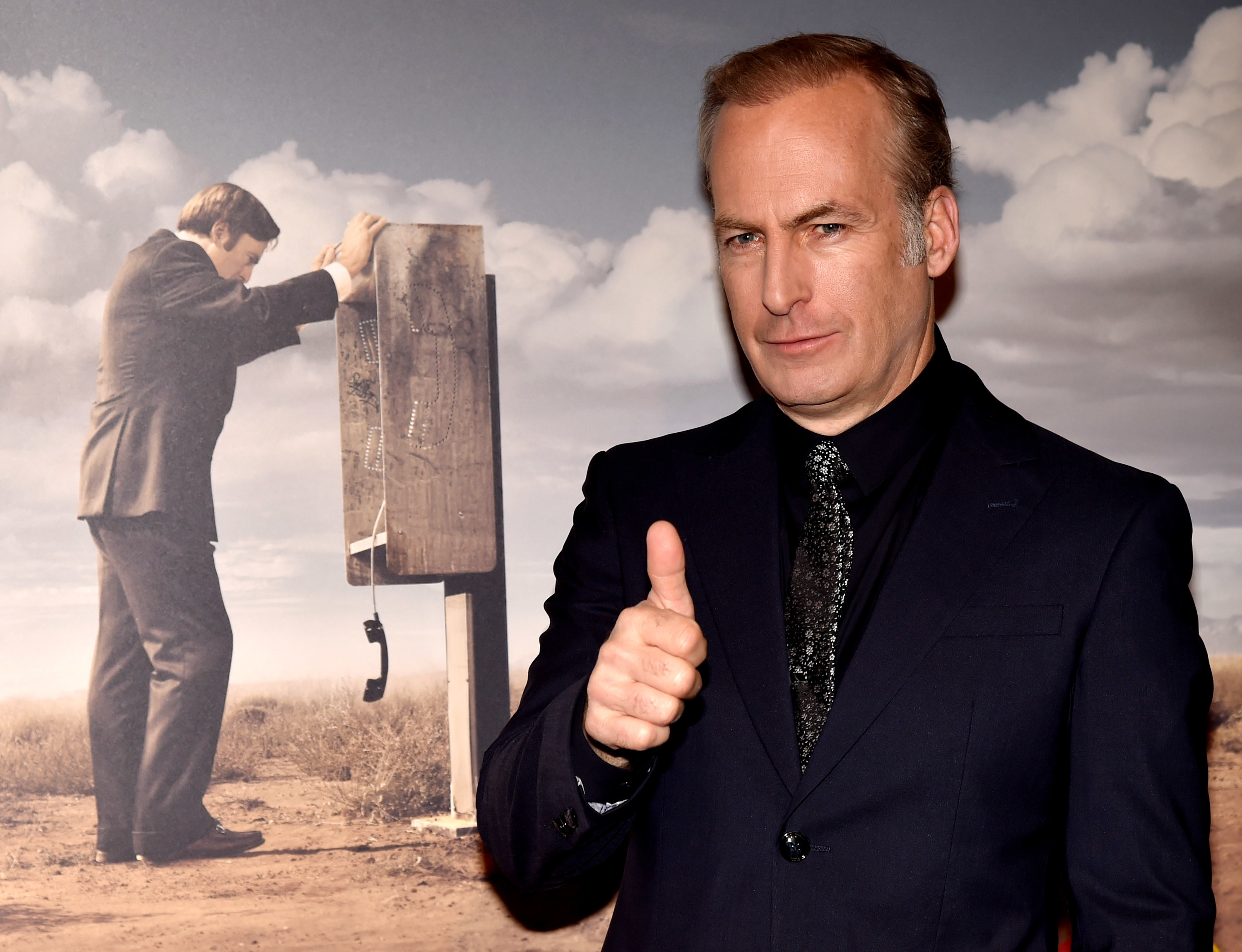 Odenkirk gives the thumbs up in front of a Better Call Saul poster