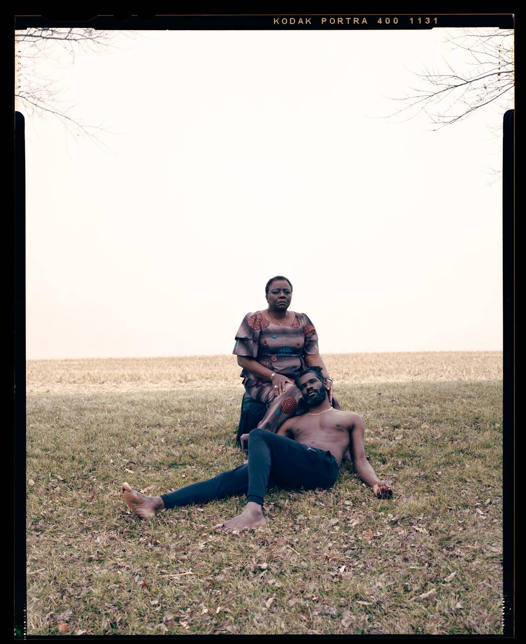 An adult son leans back and rests his head on the knee of his sitting mother