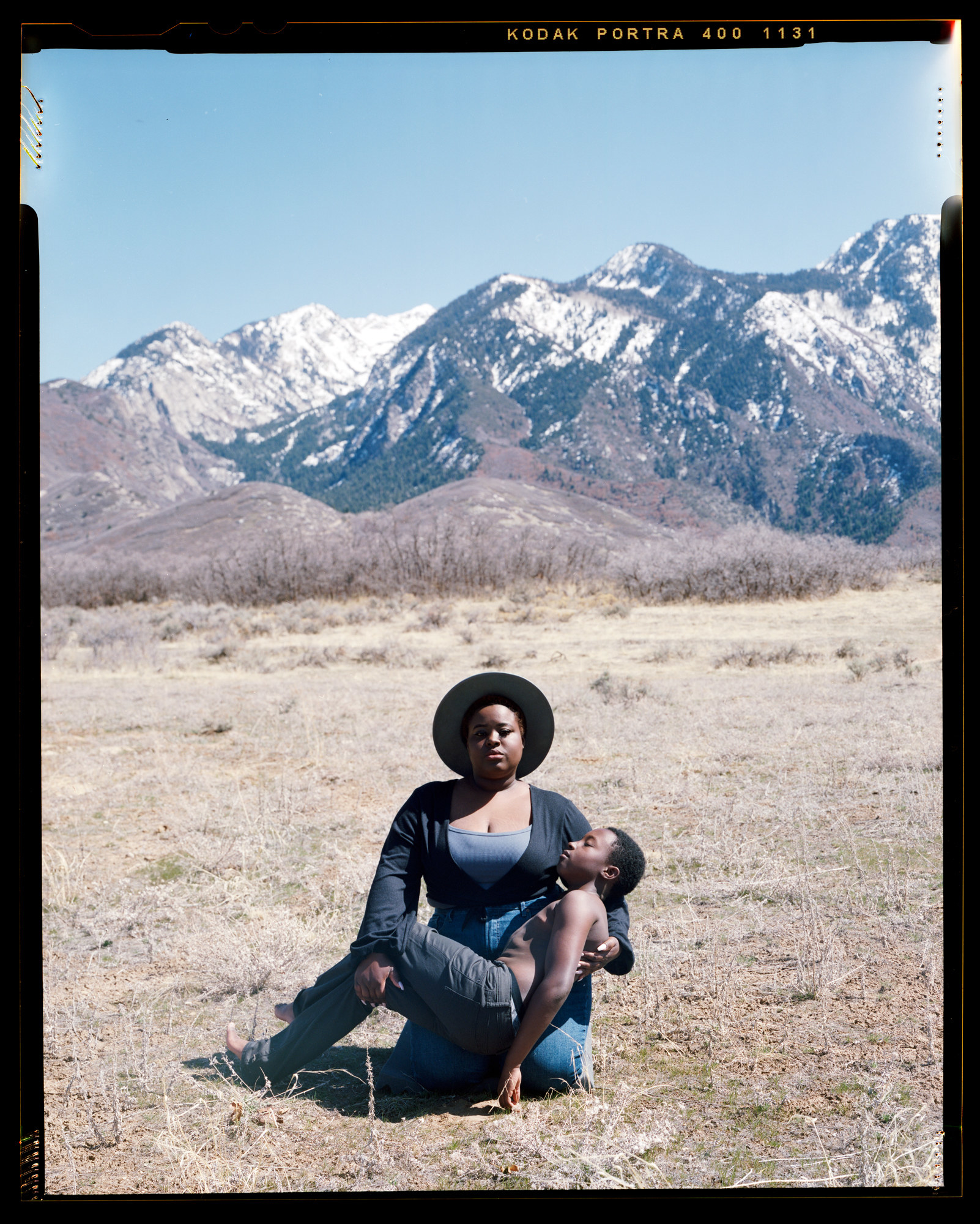 A mother holds a young son in a field in front of a mountain range