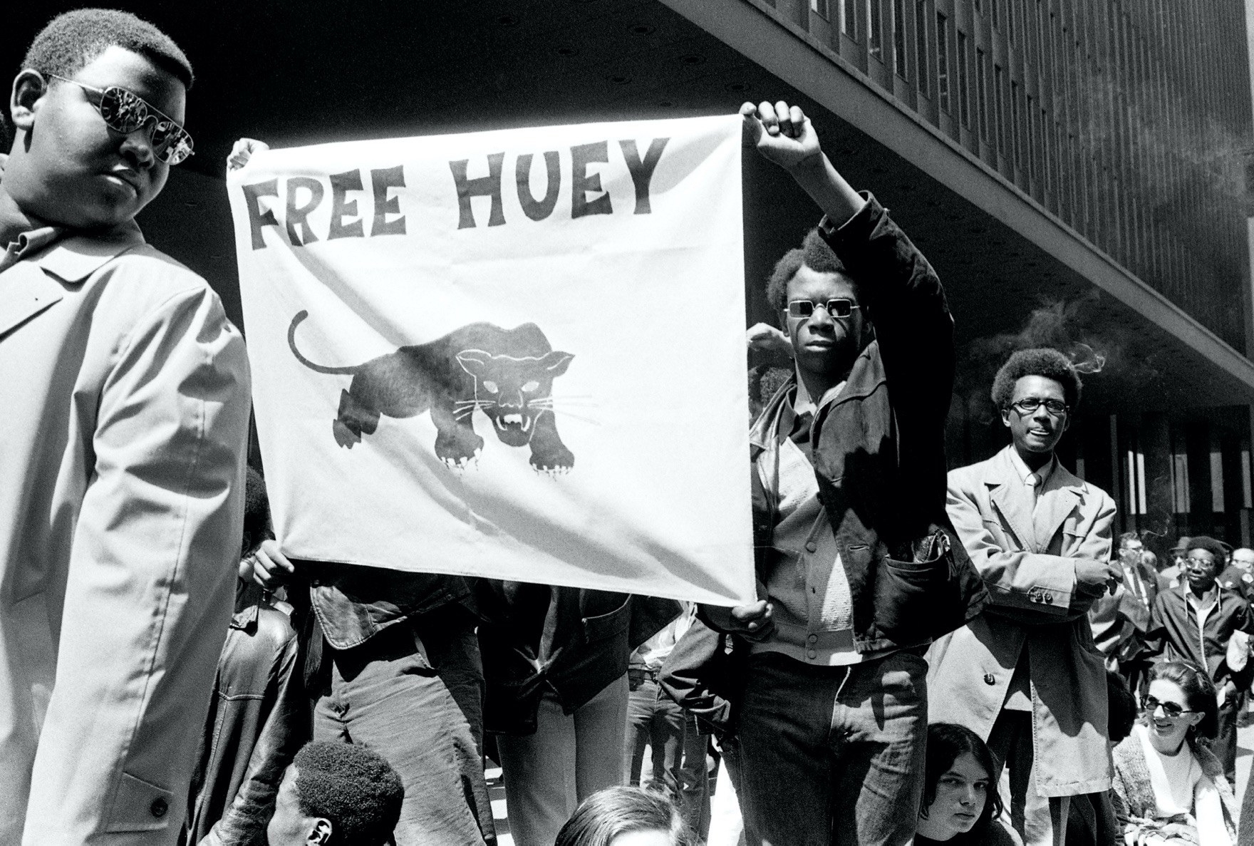 A march with men and children with a man holding up a sign that says free huey with a black panther on it
