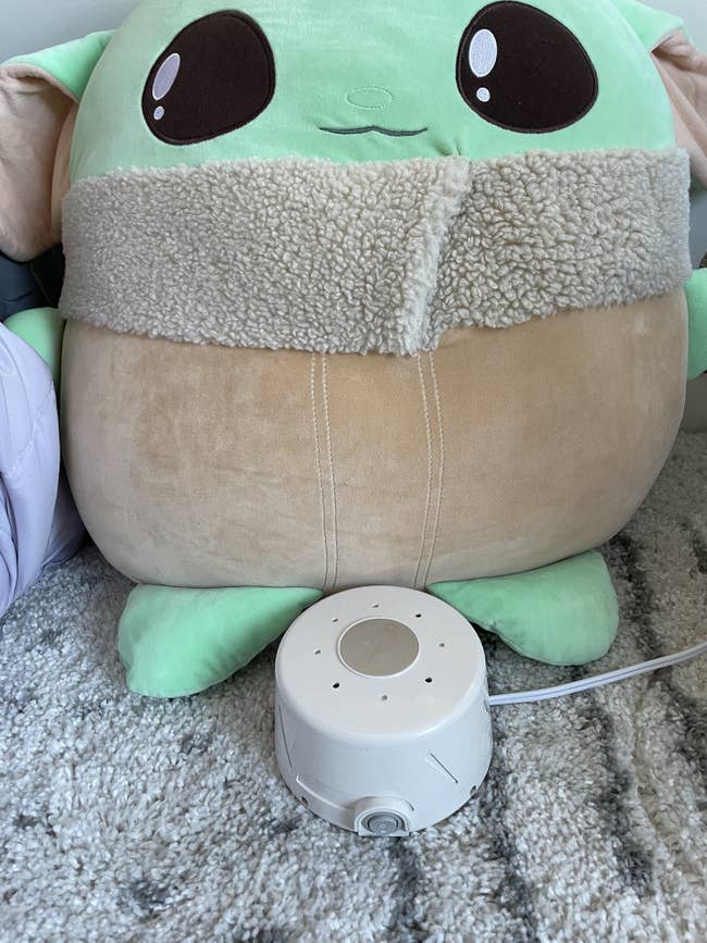 The white noise machine sitting in front of a baby yoda pillow