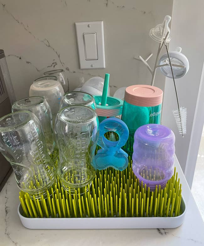 Bottles, pacifiers, and sippy cups drying on the plastic grass rack