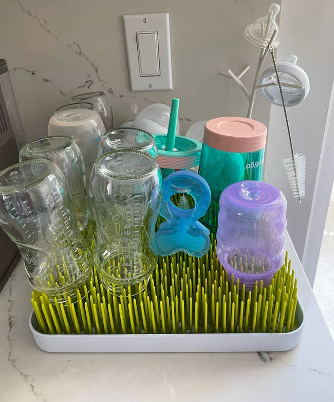 Bottles, pacifiers, and sippy cups drying on the plastic grass rack
