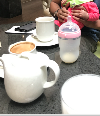 The pink baby bottle sitting on a table next to a cup of coffee