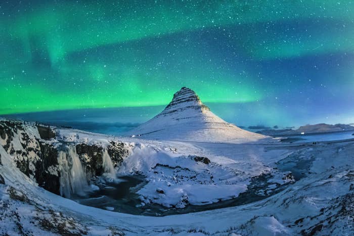 A lot of stars and green aurora over white Kirkjufell in winter after snow storm, Iceland