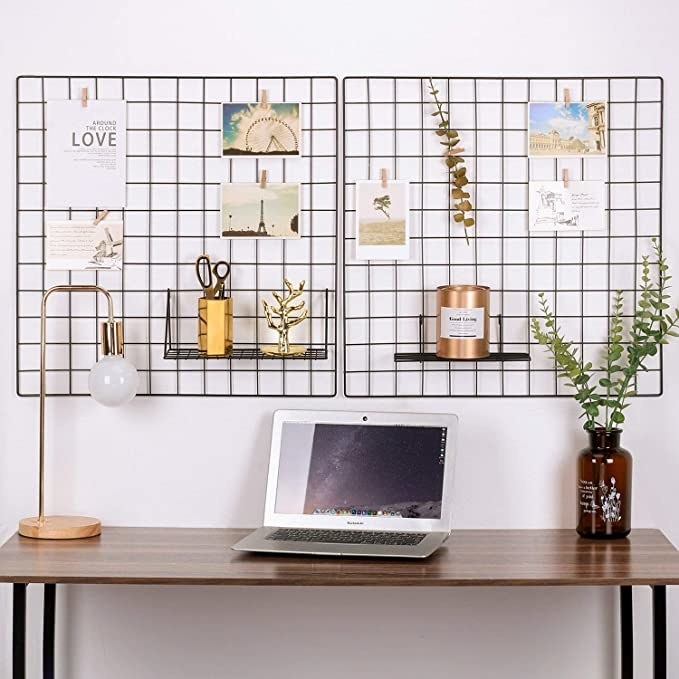 The grid boards hanging on a wall with photos and cards clipped to it above a desk with a computer, a lamp, and a vase