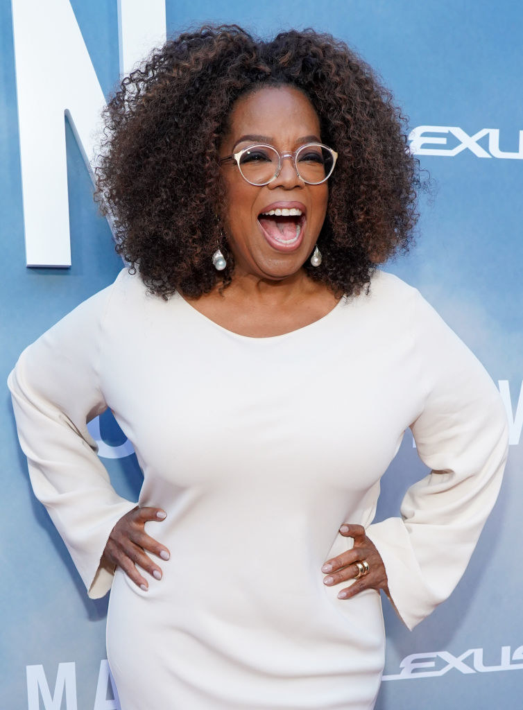 Oprah smiling with hands on hips in a slinky white dress