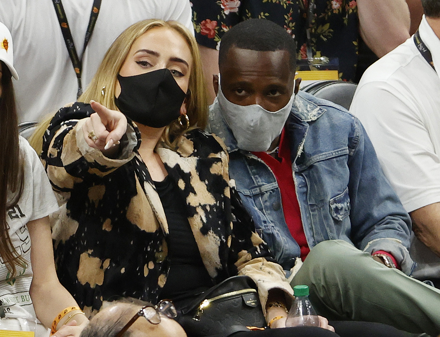 The couple sitting at a basketball game with face masks on as Adele points something out to Rich