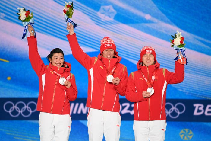 Three athletes representing China holding up their medals and small bouquets of flowers at the Beijing Olympics