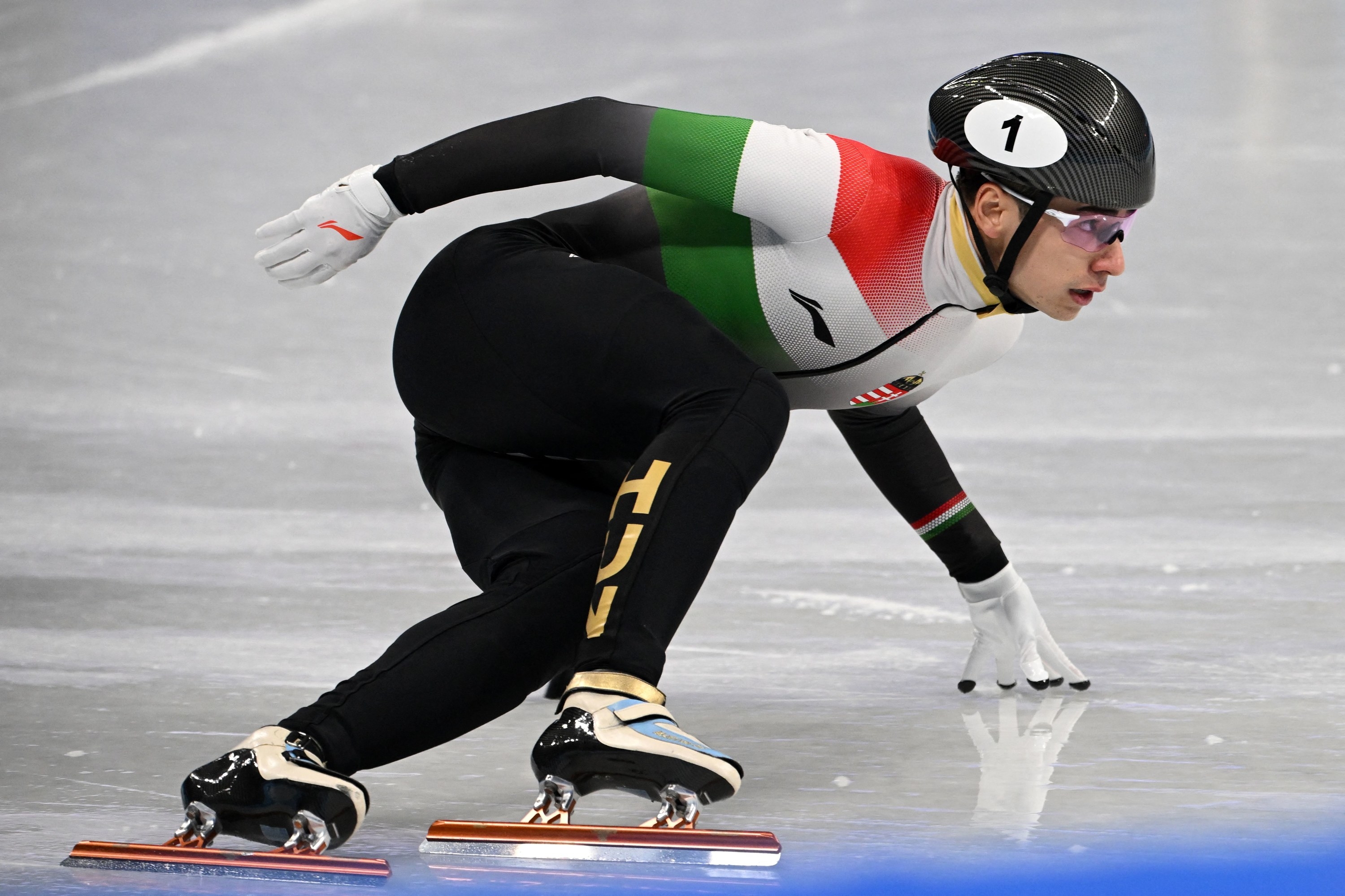 A Hungarian athlete with his hand on the ice as he rounds the corner during a short track speed skating