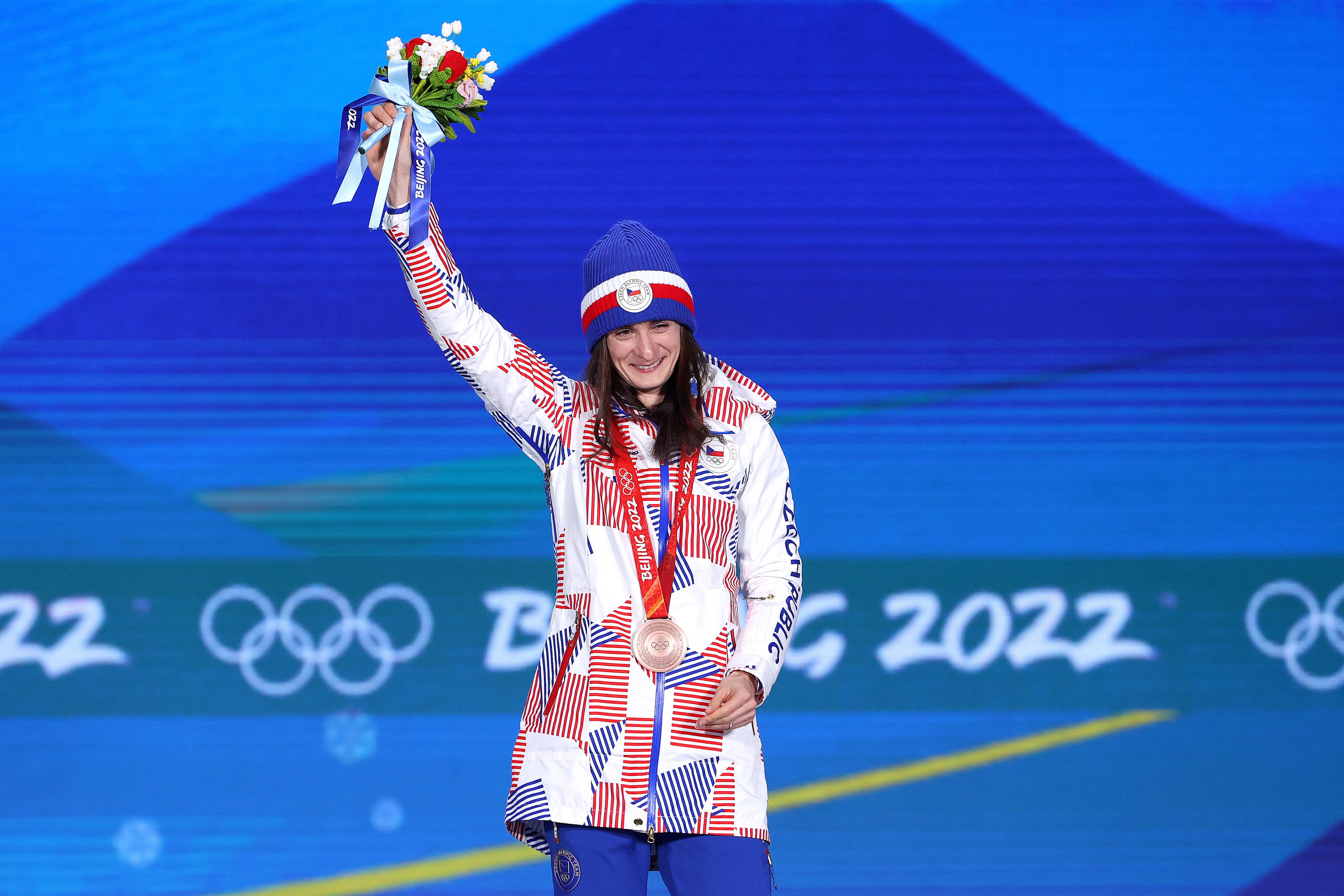 An athlete from the Czech Republic holding up her bouquet and acknowledging the crowd during the medal ceremony