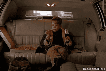 A kid eating pizza in the back of a car.