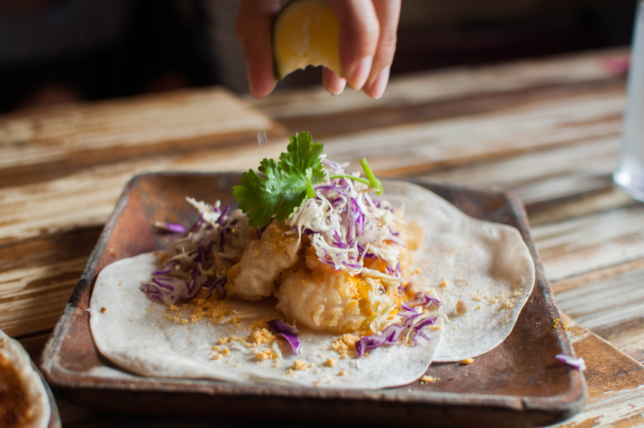 Squeezing lime on a seafood taco topped with slaw and cilantro.