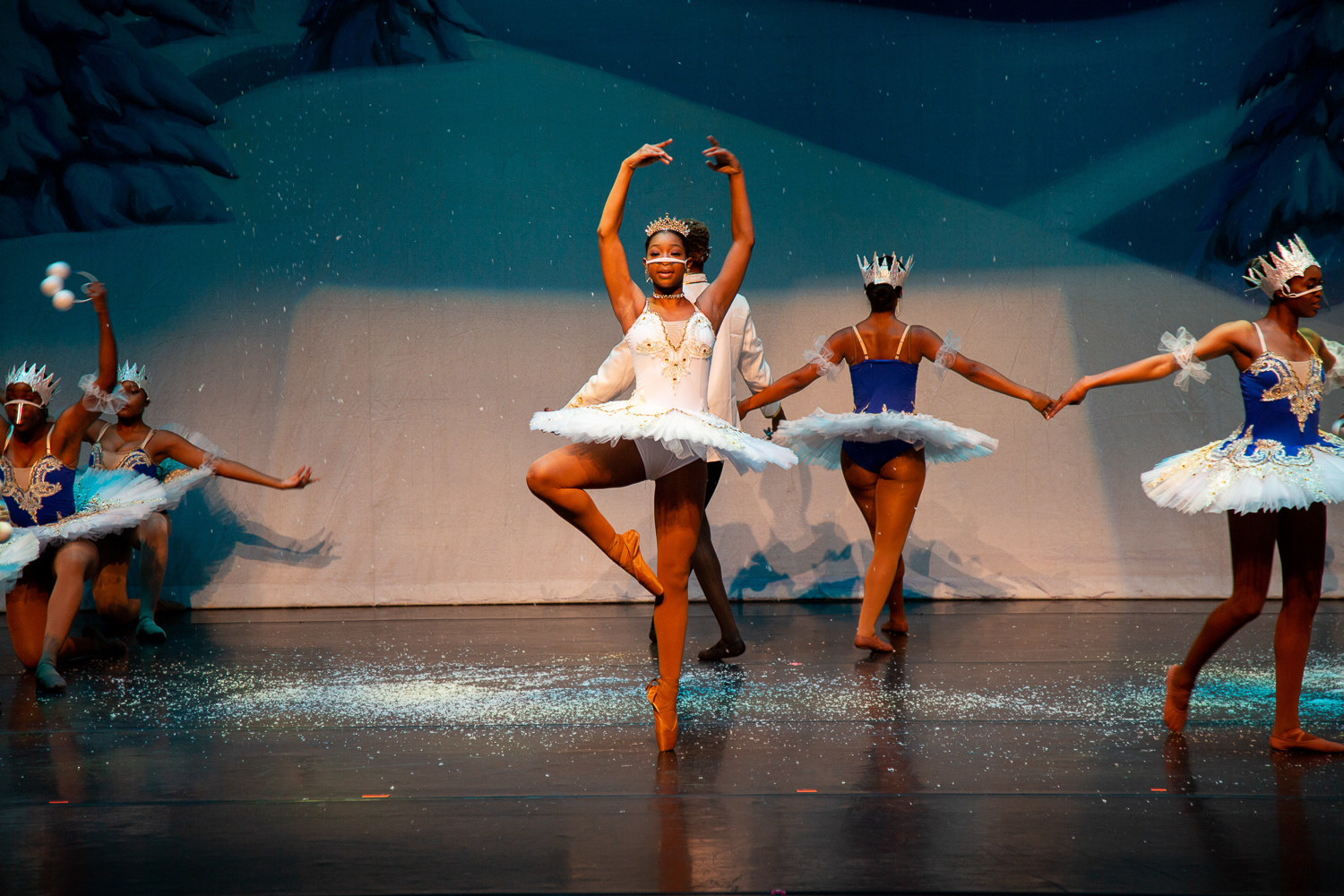 A ballerina on point on a stage covered with glitter with other dancers behind her