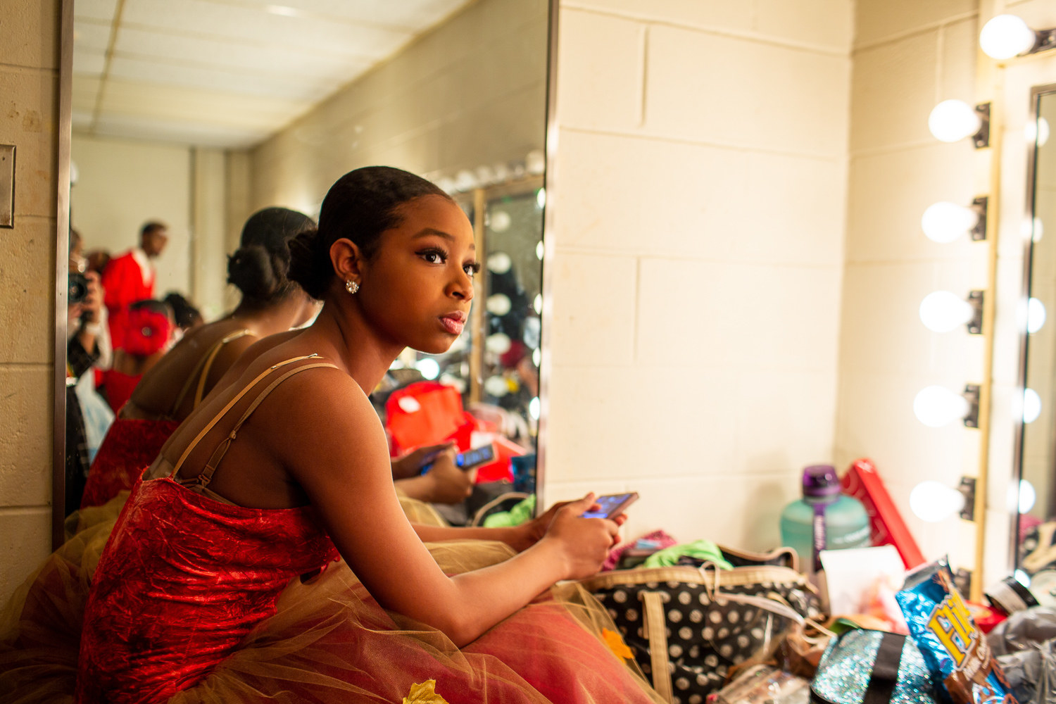 a young ballet dancer looks at her phone and watches other people get ready for the ballet