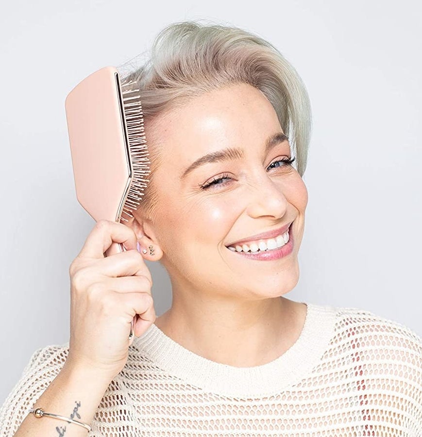 A smiling person using the paddle brush on their hair