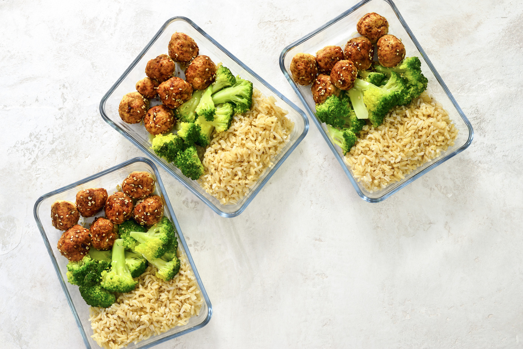 Meatballs and broccoli and rice in glass containers.
