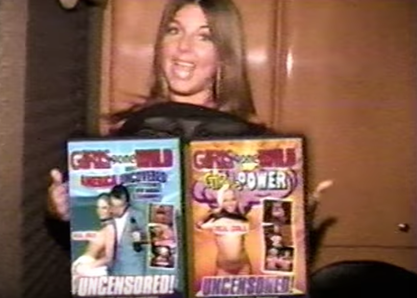 Woman flashing with two large Girls Gone Wild DVDs covering her