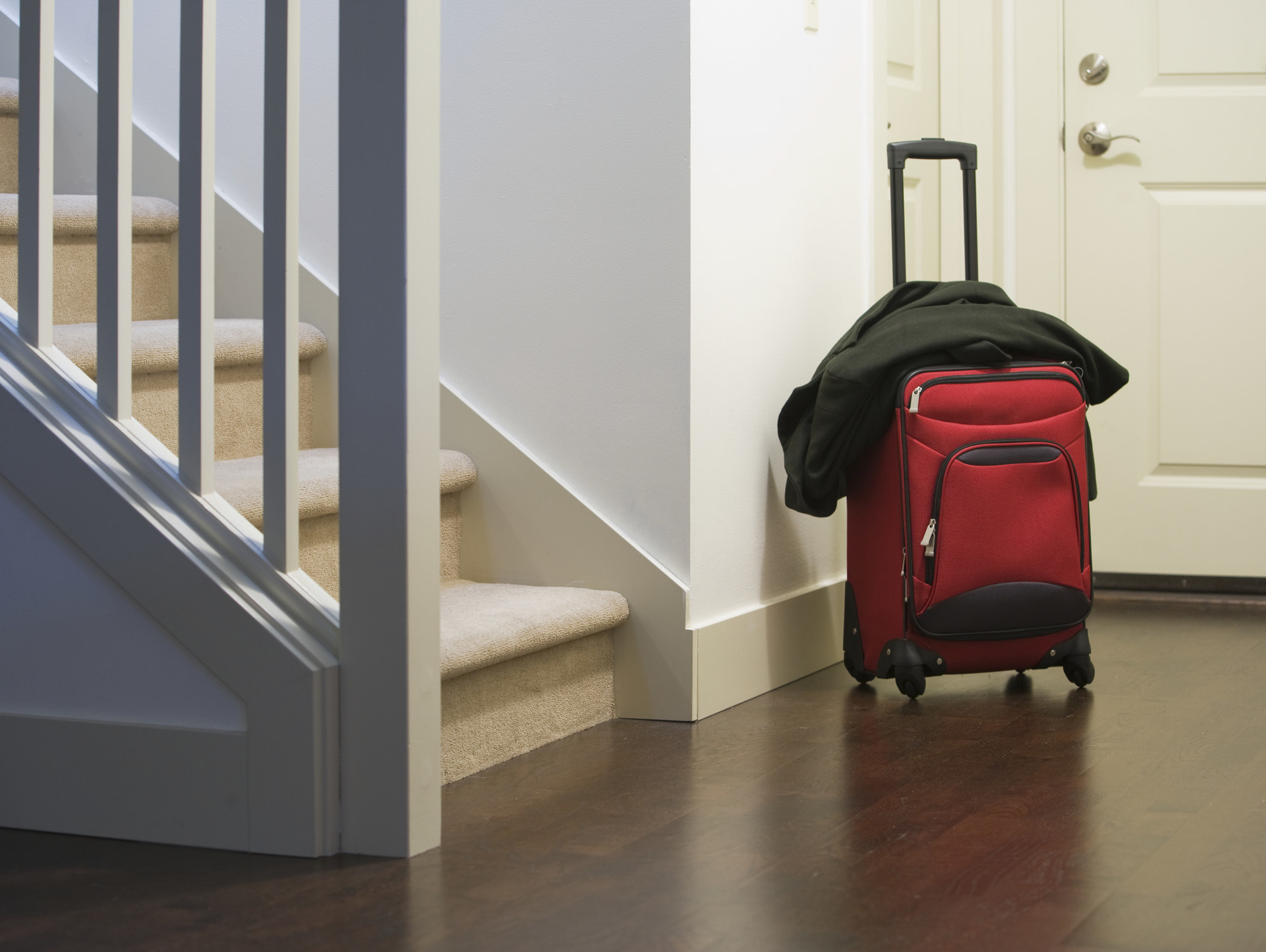 A stock image of a rolling suitcase standing by the door in a house