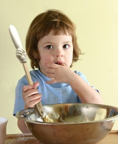 A child holding the spatula and licking some kind of batter off of their thumb