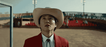 Steven Yuen in a cowboy hat looking up at something in the sky