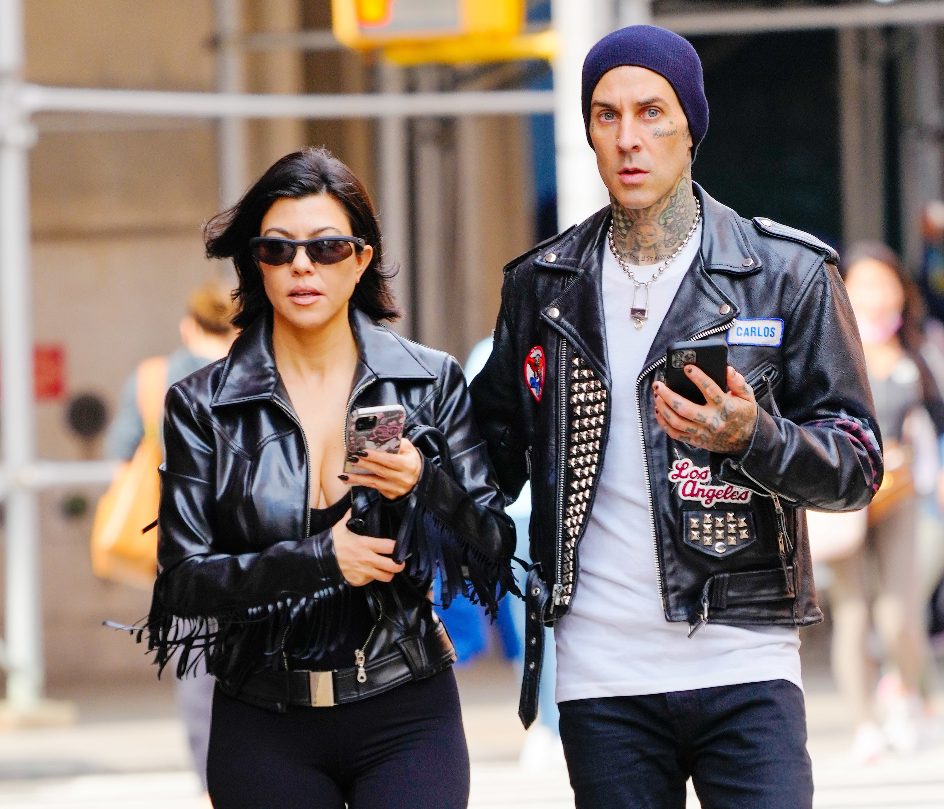Kourtney and Travis walk down the street while holding their phones