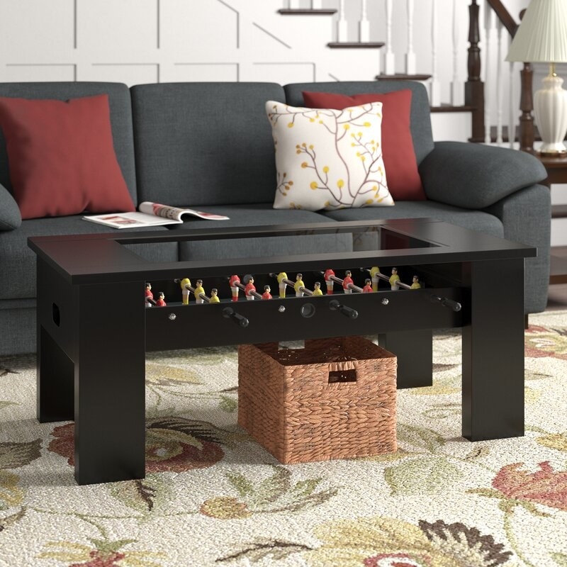Black foosball table next to a gray sofa with colorful throw pillows