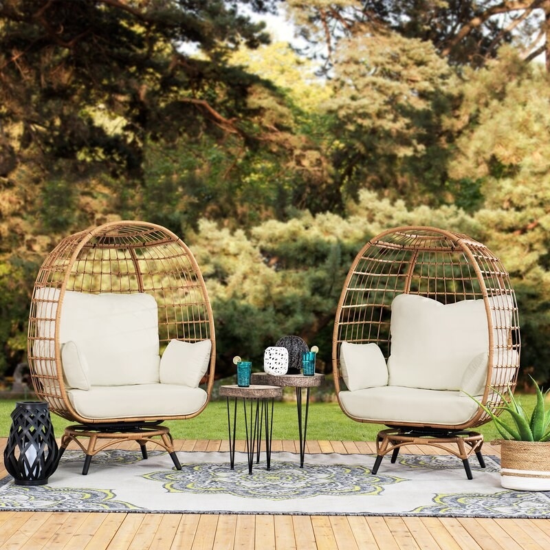 Two egg swivel chairs, end tables, plant and lantern on a rug on a patio