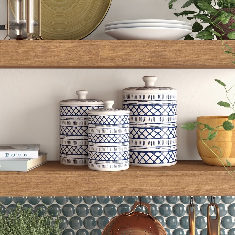 Three canisters on a shelf with other kitchen items