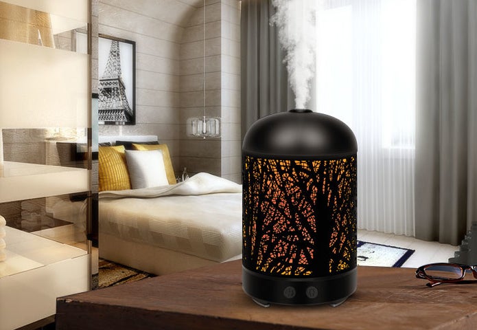 The diffuser with a tree design etched into the sides sitting on a table in a bedroom