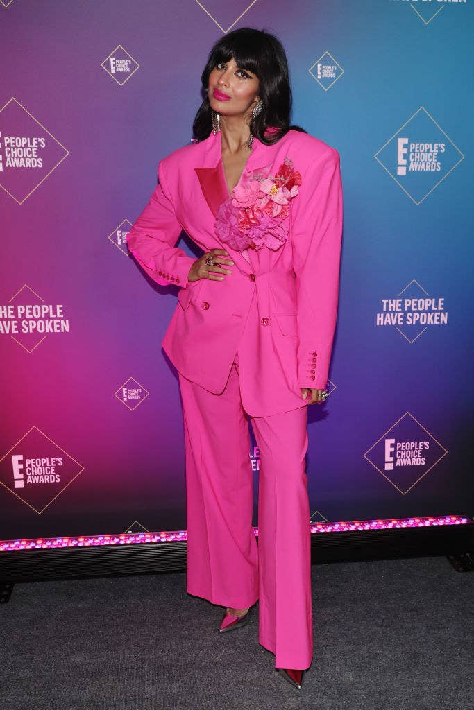 dressed in a bold suit adorned with flowers, Jameela poses with her hand on her hip on the red carpet