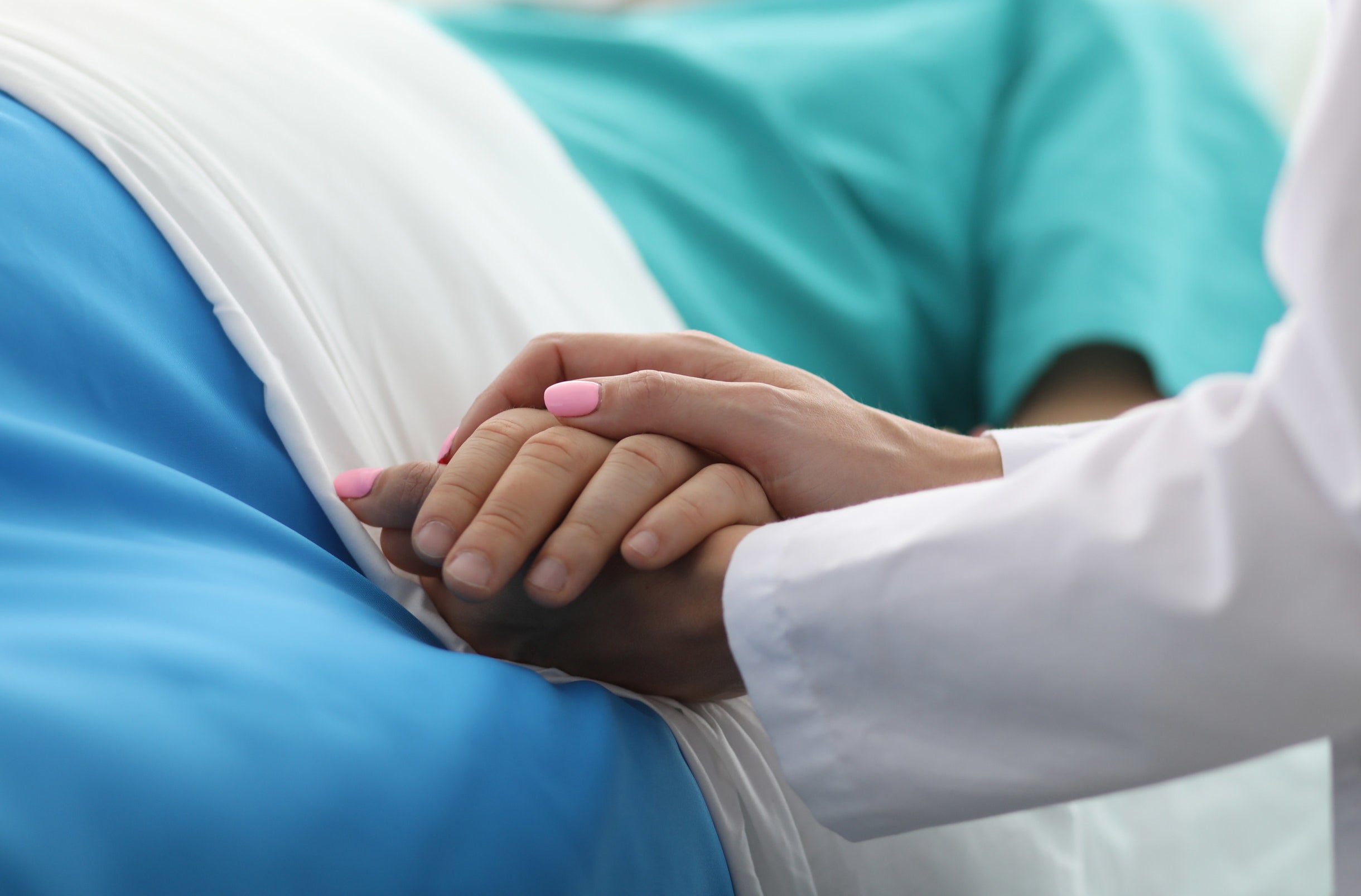 a doctor holds a patient&#x27;s hand while they lie in bed