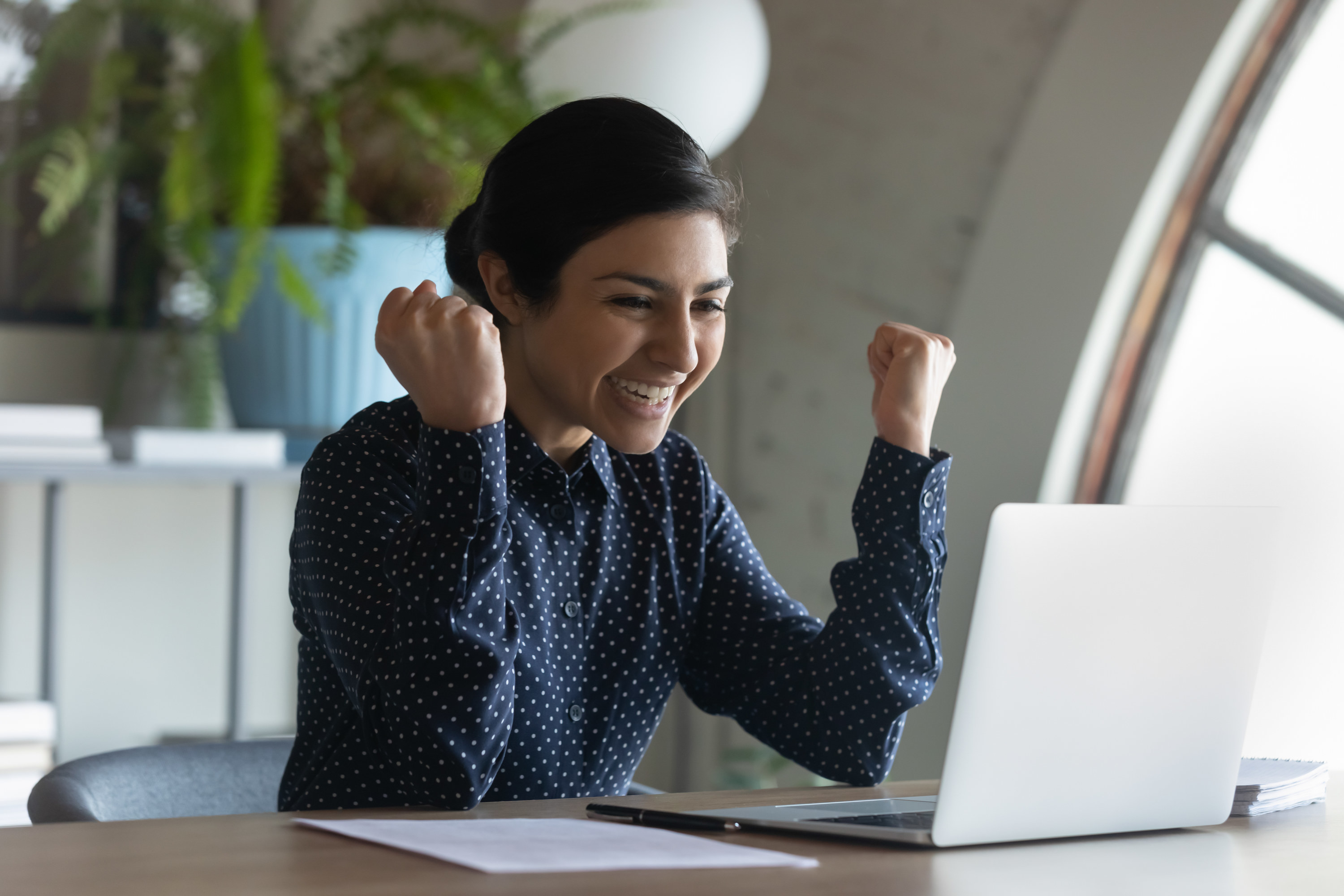 Woman celebrating at her desk after negotiating higher pay