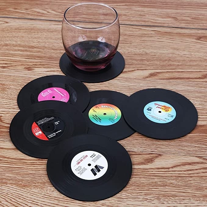 The set of six vinyl coasters on a wooden table with a stemless wine glass sitting on one of them