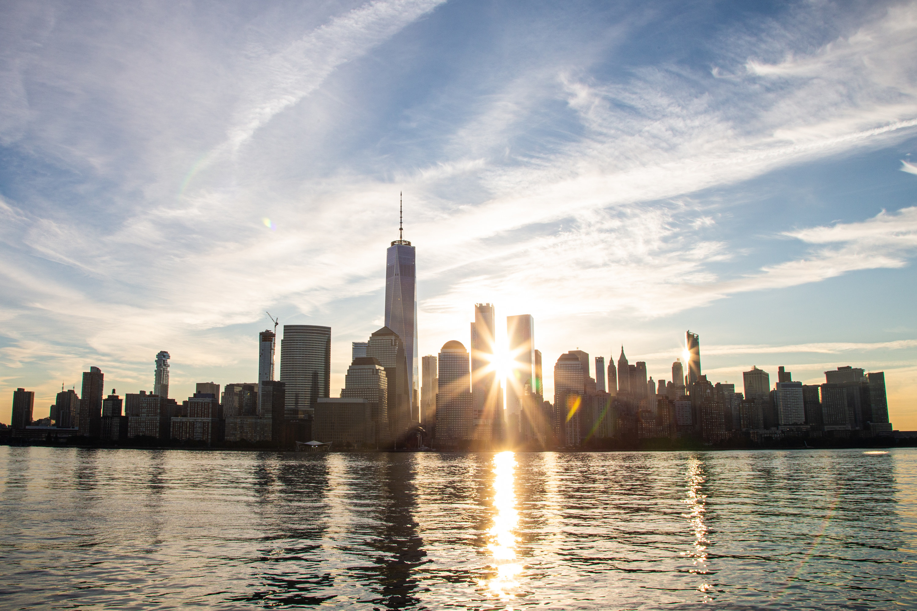 The sunset shining through the New York City skyline, photographed from the water